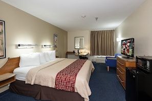 A hotel room with a bed, a desk with a television, a chair, a desk lamp, and a window with curtains. - Red Roof Inn Jackson, OH (Jackson)