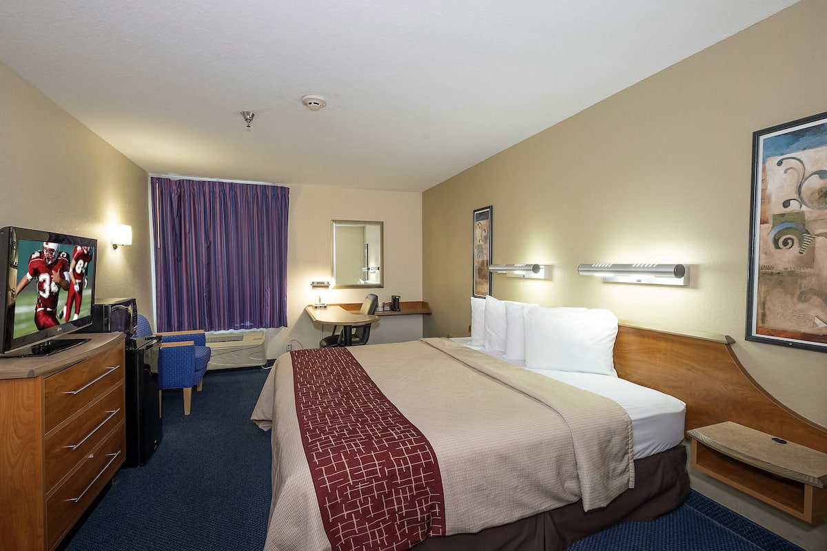 A hotel room with a large bed, a desk with a chair, a television, and a bathroom with a shower.