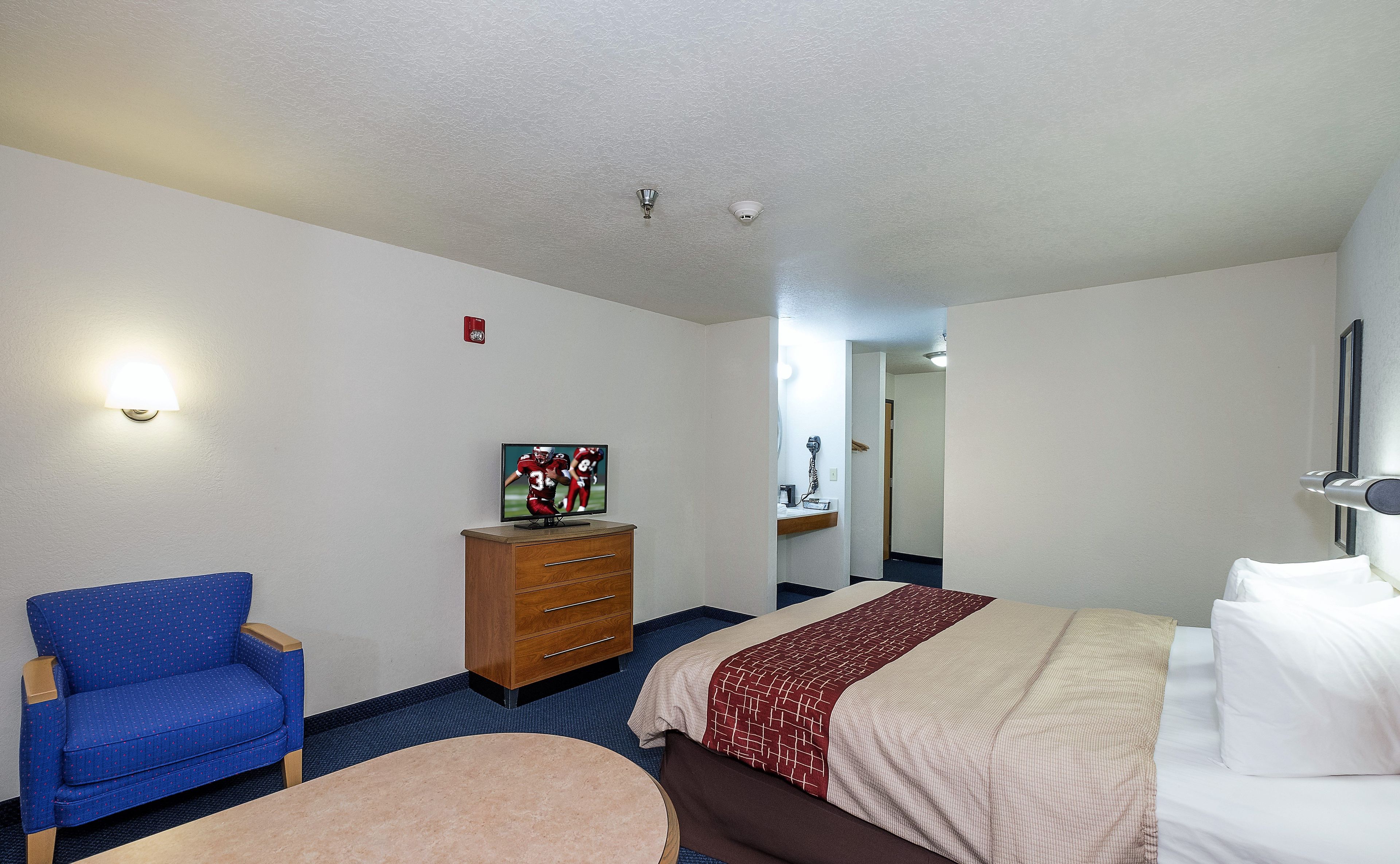Une chambre d’hôtel avec un lit, une commode, une chaise, un téléviseur et une salle de bain visible au fond.