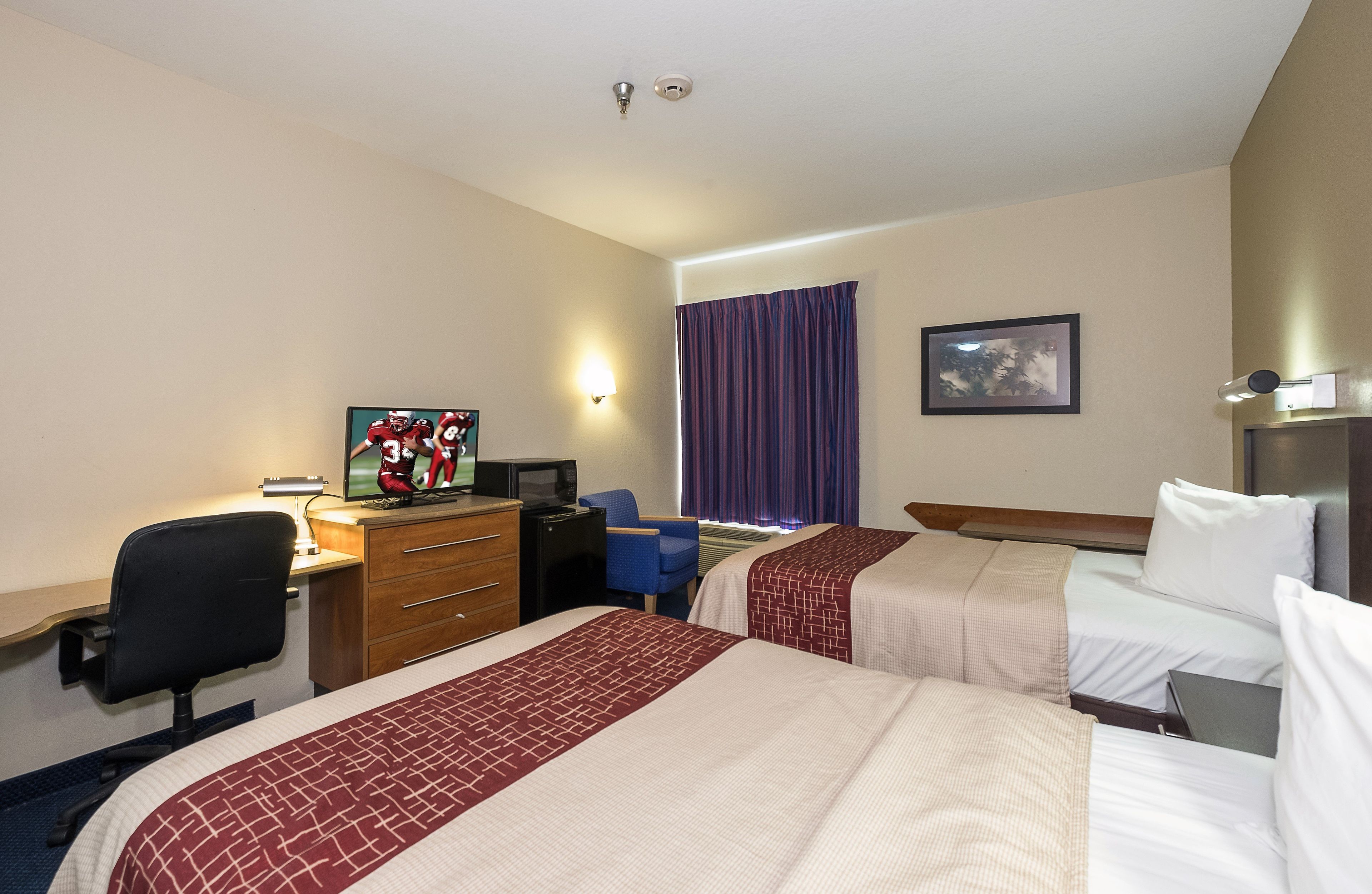 Habitación de hotel con dos camas, un escritorio con computadora, una silla, un televisor y un cuadro en la pared.