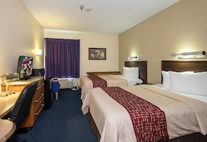Quarto de hotel com duas camas, uma escrivaninha com computador, uma cadeira, televisão e janela com cortinas.
