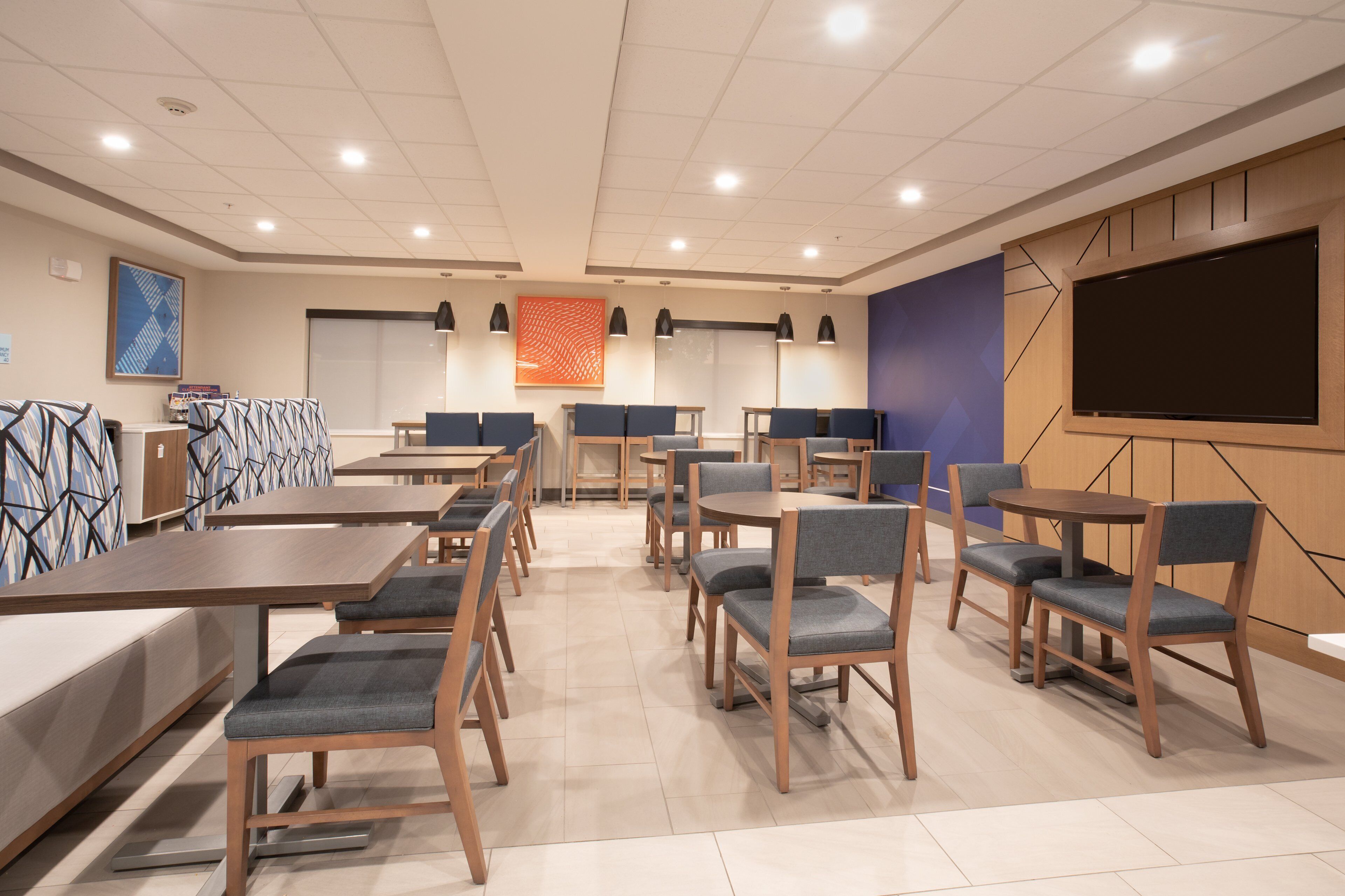 A conference room with multiple tables and chairs, a large screen, and a projector.
