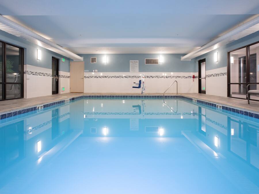 A large indoor swimming pool with clear blue water, tiled walls, and a pool ladder.