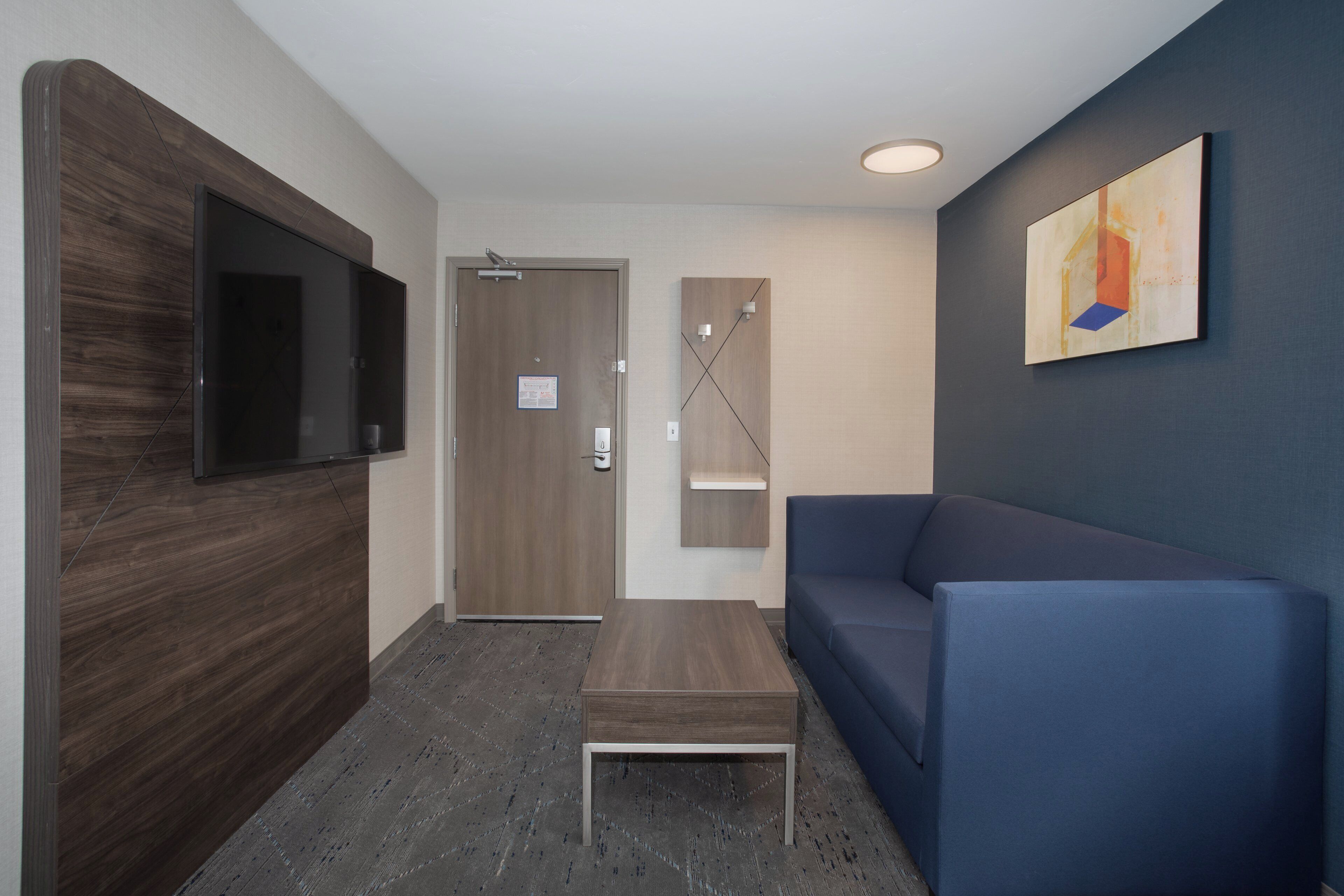 A modern lobby with a flat-screen TV, a wooden reception desk, a blue sofa, and a painting on the wall.