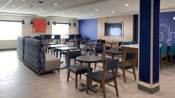 Un comedor moderno con varias mesas y sillas, una pantalla grande y una pared azul decorativa.