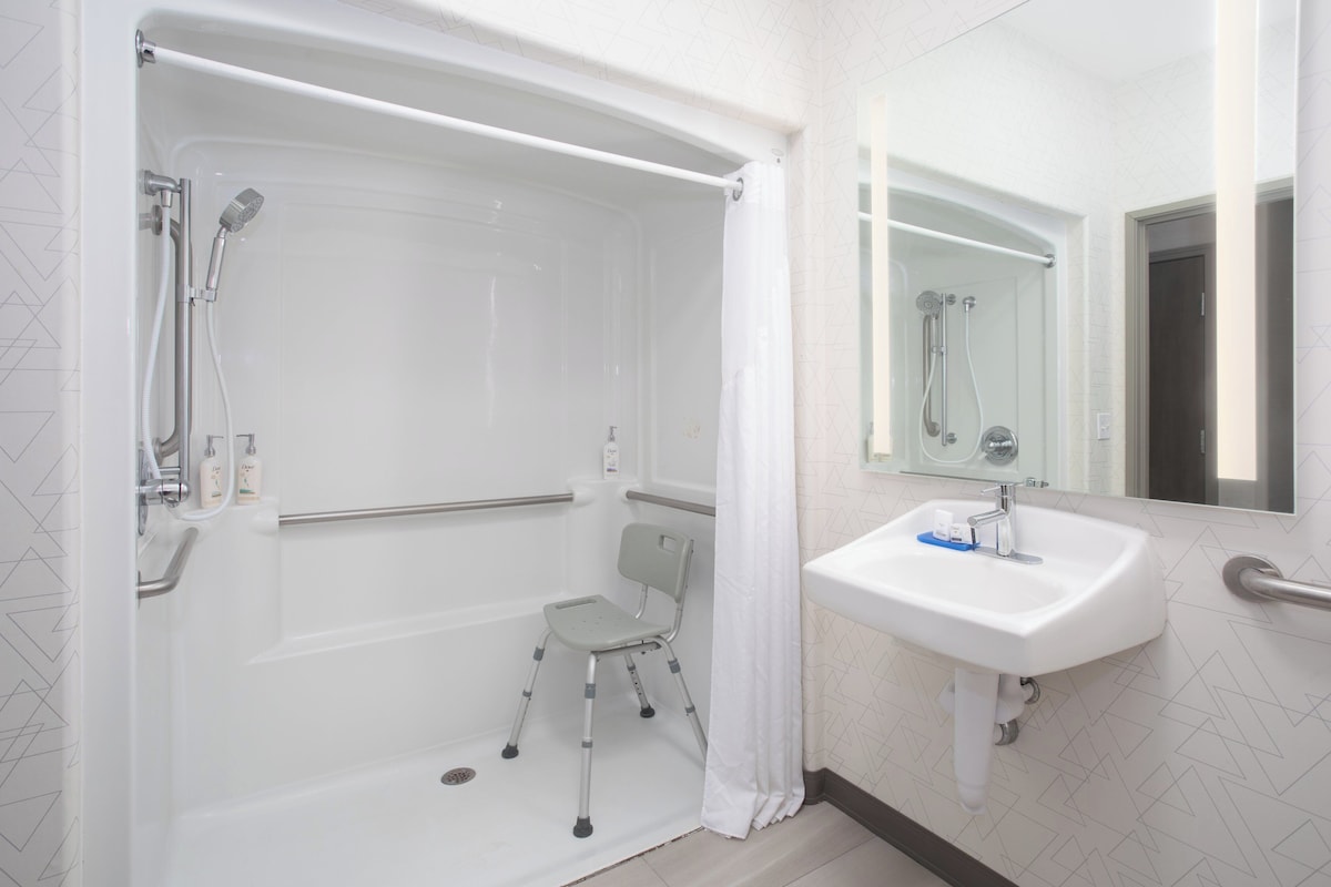 A modern bathroom with a walk-in shower, grab bar, and a sink with a mirror.