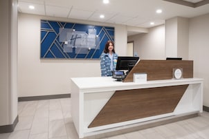 A hotel reception desk with a modern design, a digital kiosk, and a sign indicating the hotel name.