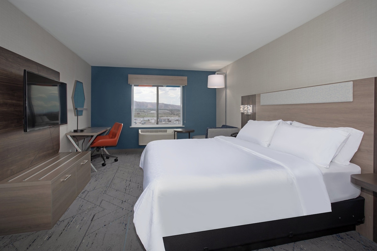 A hotel room with a bed, desk, chair, and a large window offering a view.