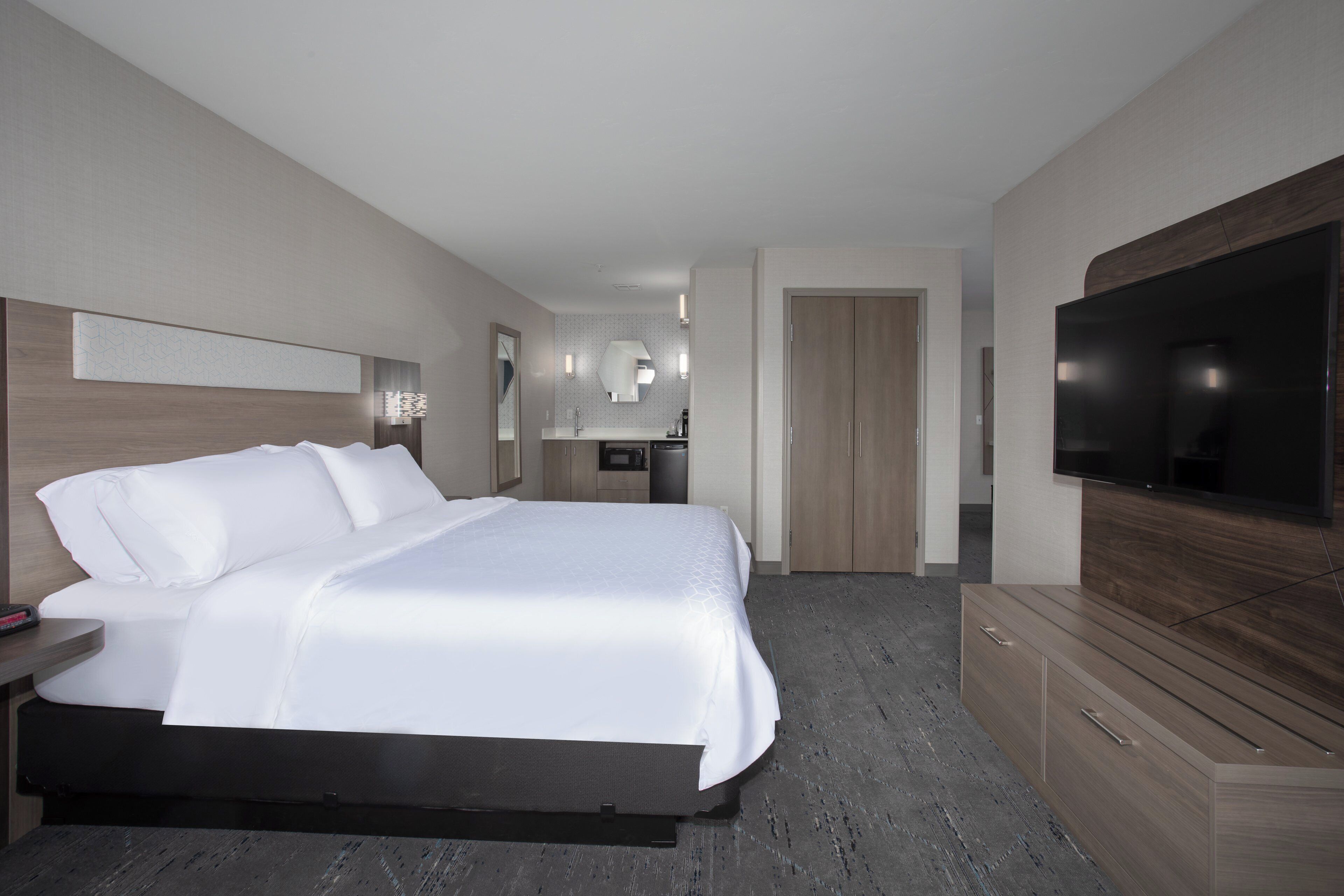 A hotel room with a large bed, a TV, a desk with a mirror, and a wardrobe.