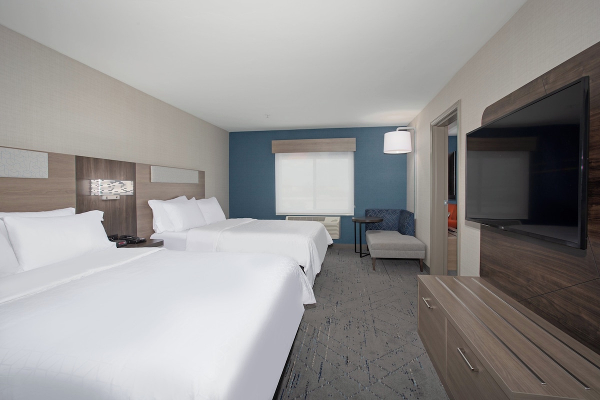 A hotel room with two beds, a television, a small table, and a chair.