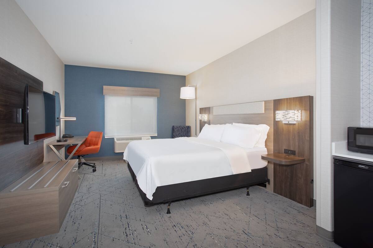 A modern hotel room with a bed, desk, chair, and a television.