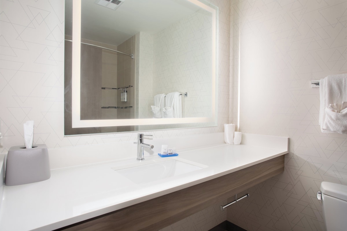 A modern bathroom with a large mirror, white sink, and wooden vanity.