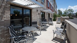 An outdoor patio with metal chairs and tables, a brick building, and a parking lot in the background. - Holiday Inn Express & Suites Grand Junction by IHG (Grand Junction)