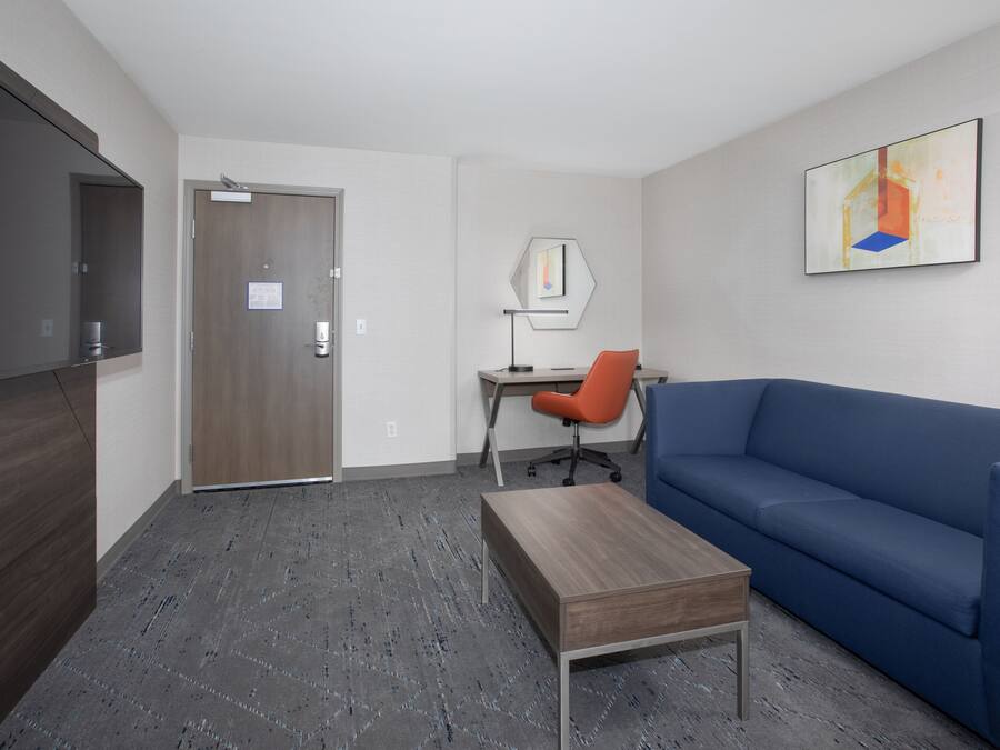 Una habitació d'hotel moderna amb escriptori de fusta, sofà blau, televisió de pantalla plana i un quadre a la paret.