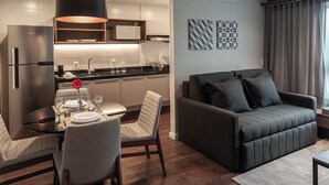 A modern living room with a dark grey sofa, a dining table set with plates and glasses, a kitchen area with a microwave, and a large window with curtains. - Slaviero Porto Alegre (Porto Alegre)