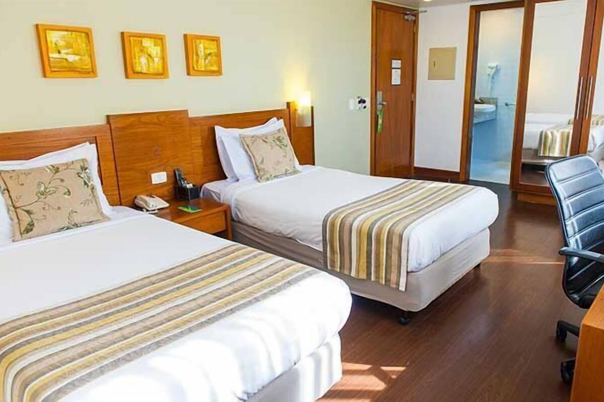 Habitación de hotel con dos camas, un escritorio y una silla. Hay tres cuadros en la pared.
