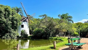 A traditional windmill by a calm river, surrounded by lush greenery and picnic tables. - Slaviero Porto Alegre (Porto Alegre)