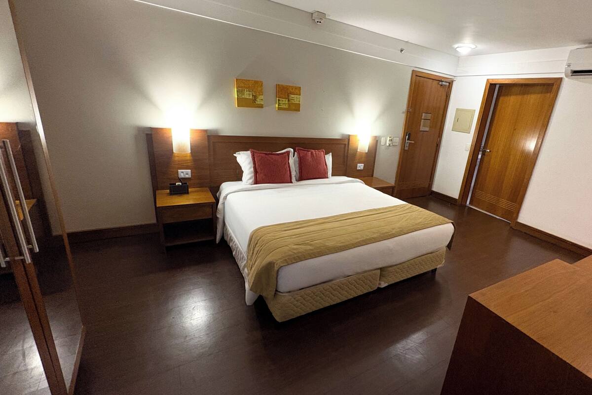 Una habitación de hotel con una cama grande, mesitas de noche, un escritorio y un equipo de aire acondicionado.