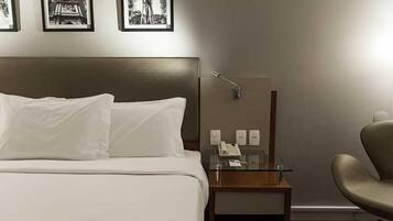 A hotel room with a bed, a nightstand with a lamp, a chair, and a wall-mounted telephone.