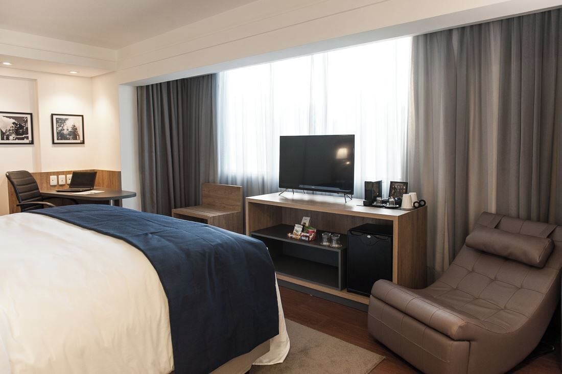 A hotel room with a bed, a desk with a TV, a chair, and a sofa.