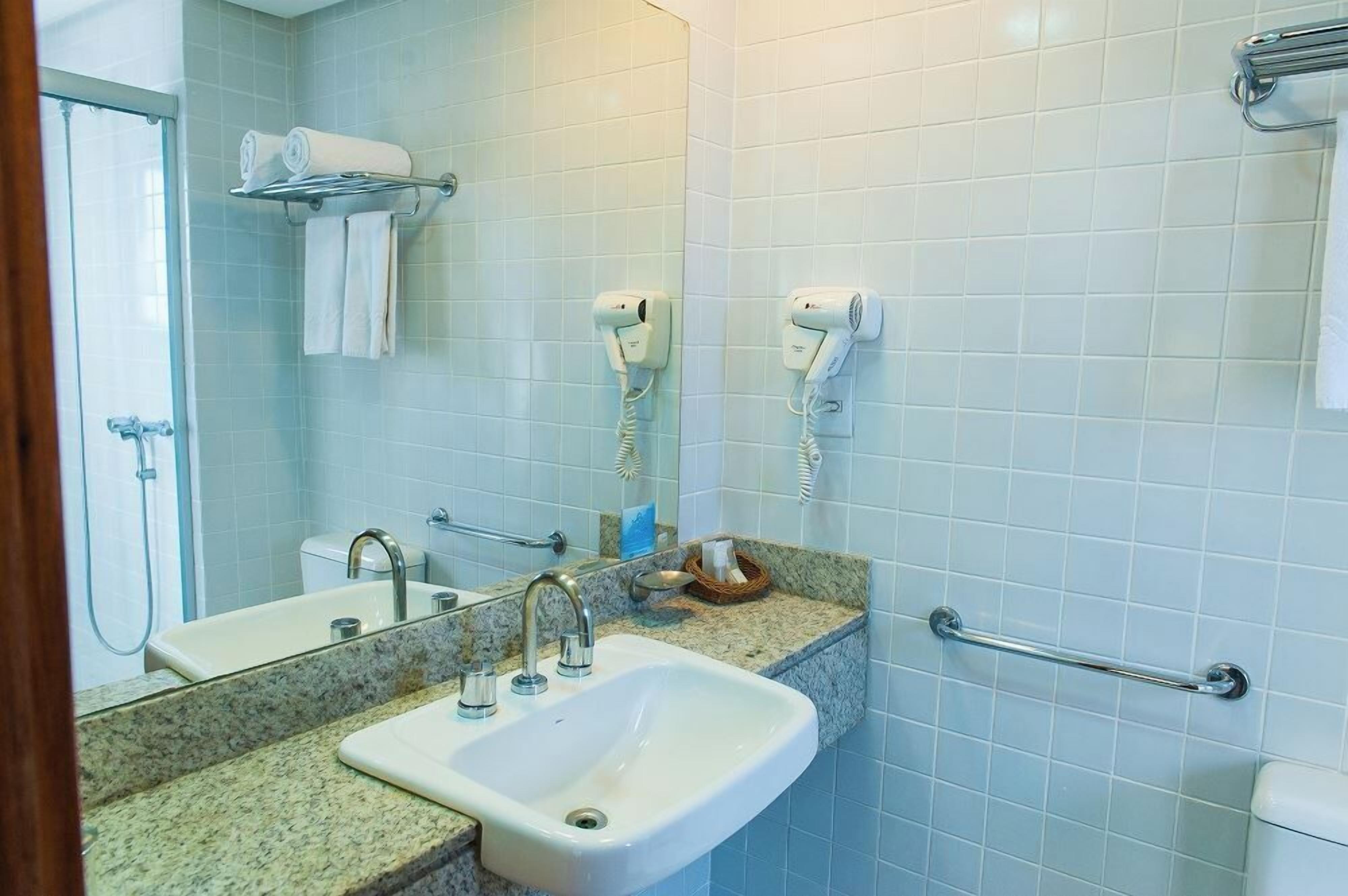 A bathroom with a sink, mirror, towel rack, and two hair dryers.