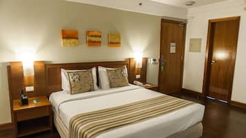 Habitación de hotel con una cama grande, cabecero de madera, dos mesitas de noche y una puerta.
