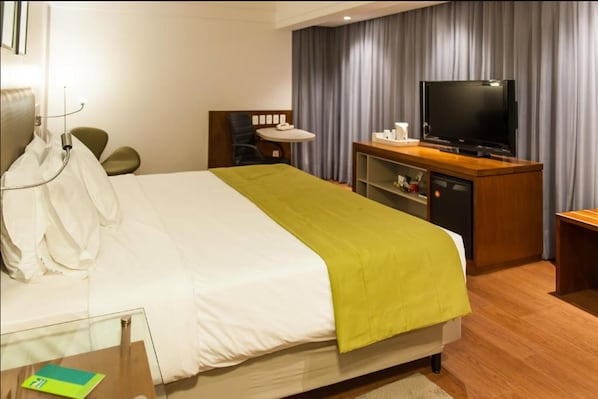 A hotel room with a bed, a television, a desk with a chair, and a curtain backdrop.