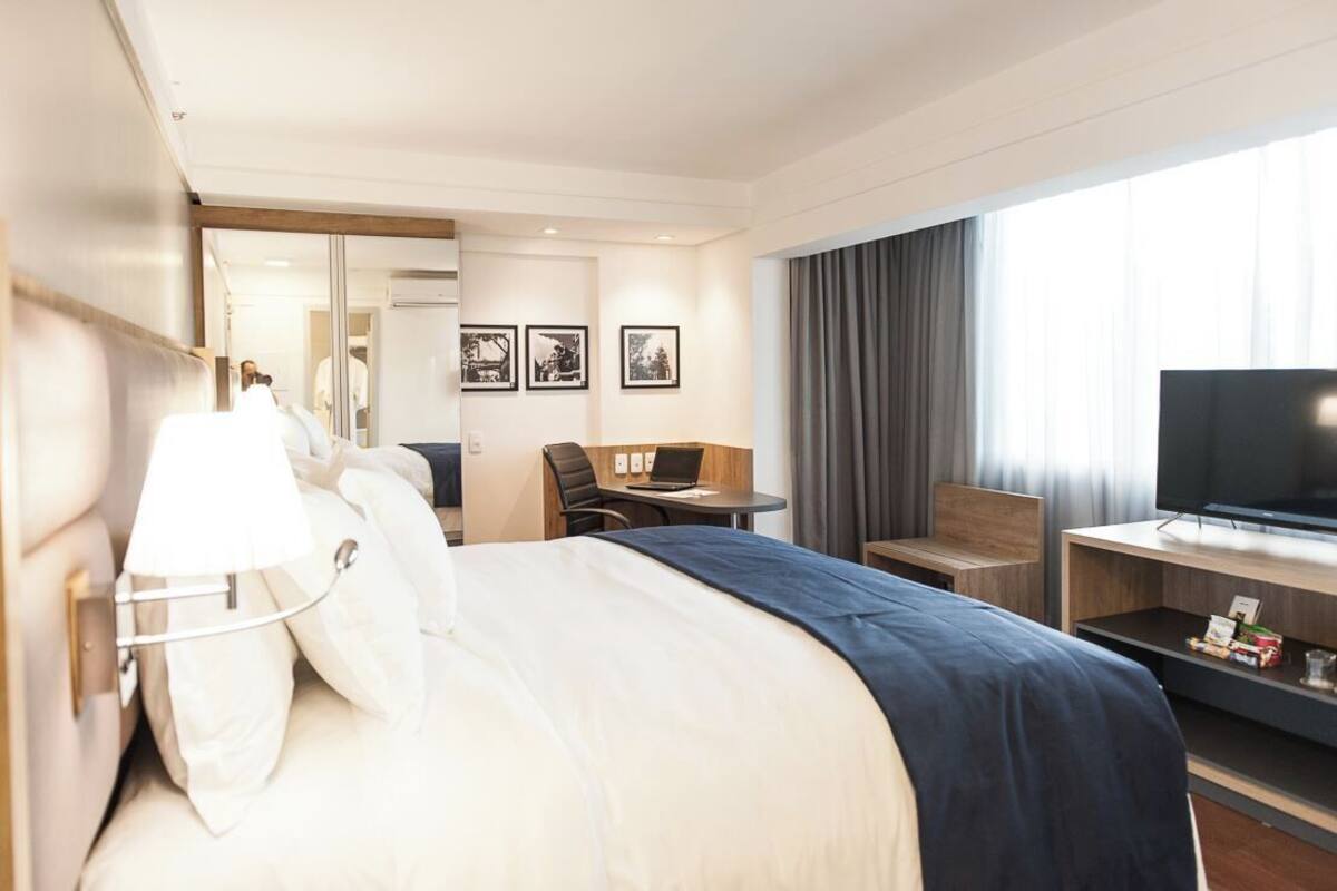 Habitación de hotel con una cama grande, un escritorio con una computadora portátil, un televisor y cuadros en la pared.