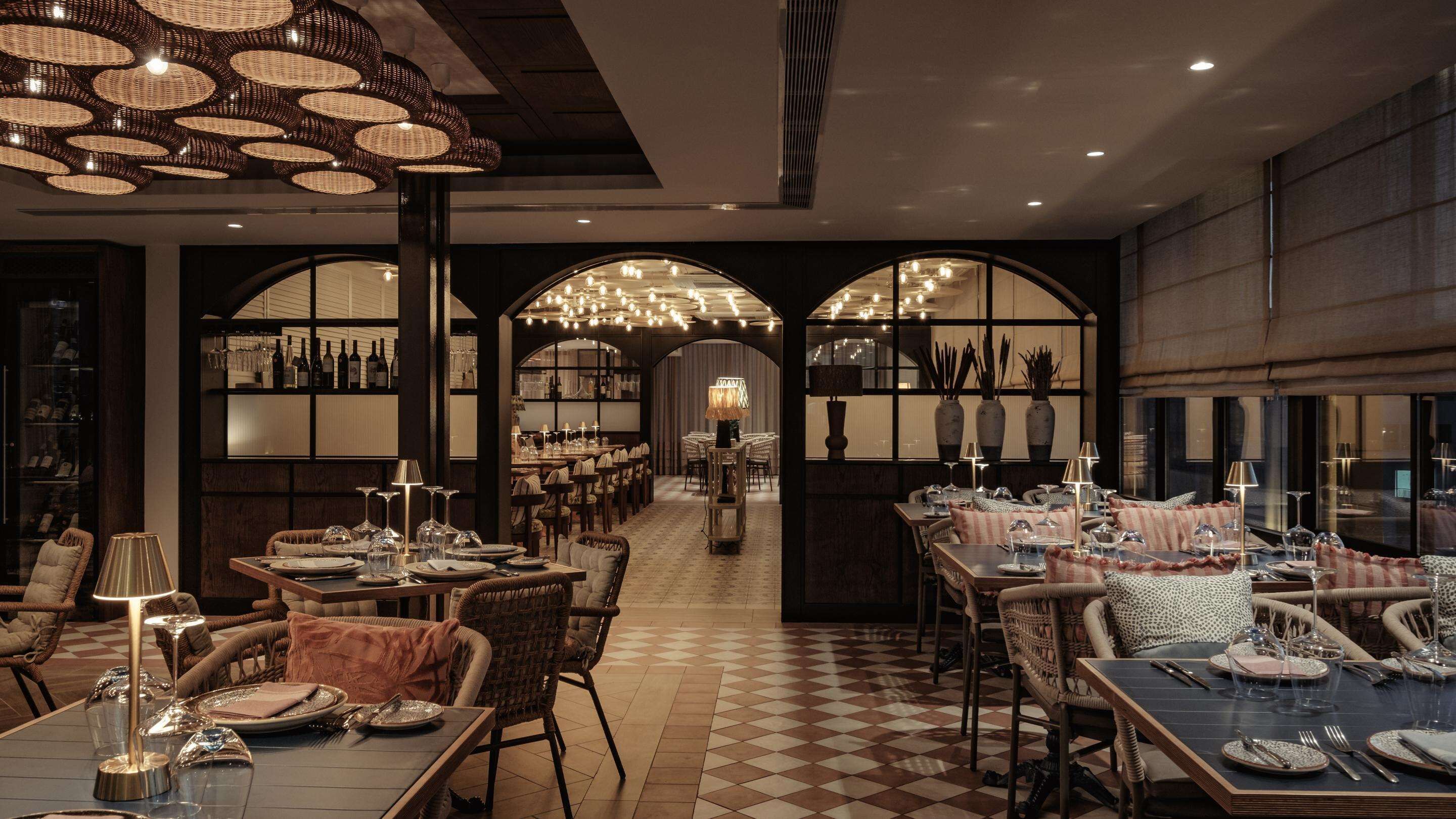 A restaurant with a checkered floor, wicker chairs, and tables set for dining.