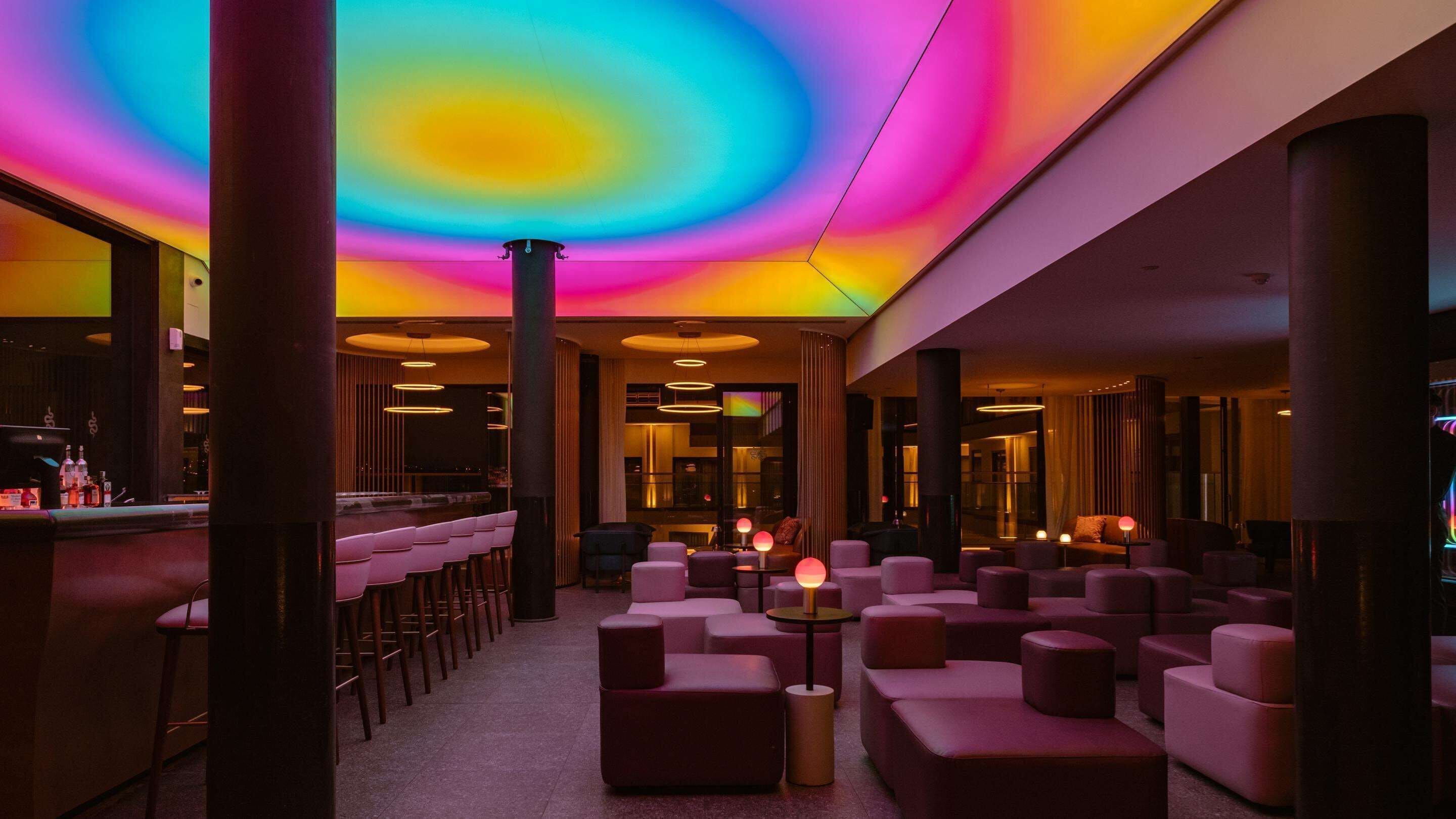 A modern lounge area with a vibrant ceiling, multiple seating options, and a bar counter.