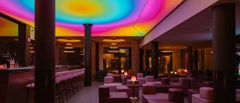 A modern lounge area with a vibrant ceiling, multiple seating options, and a bar counter.