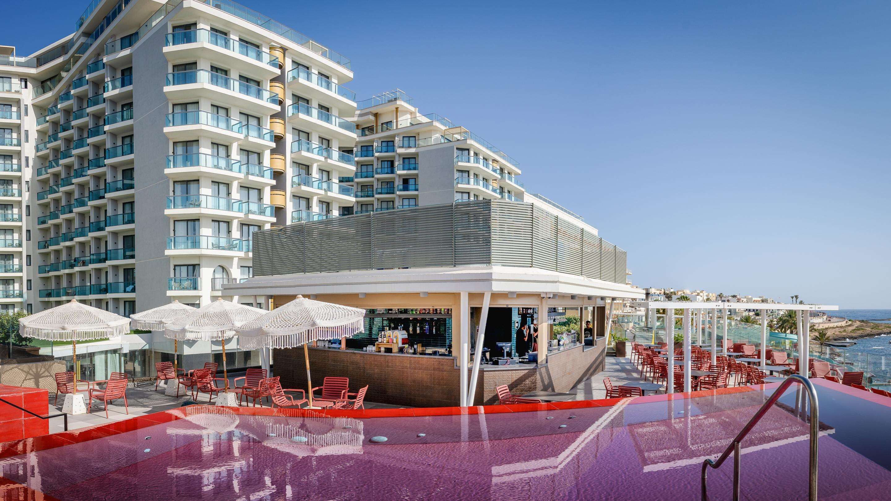 A rooftop bar with outdoor seating, a pool, and a view of a high-rise building.