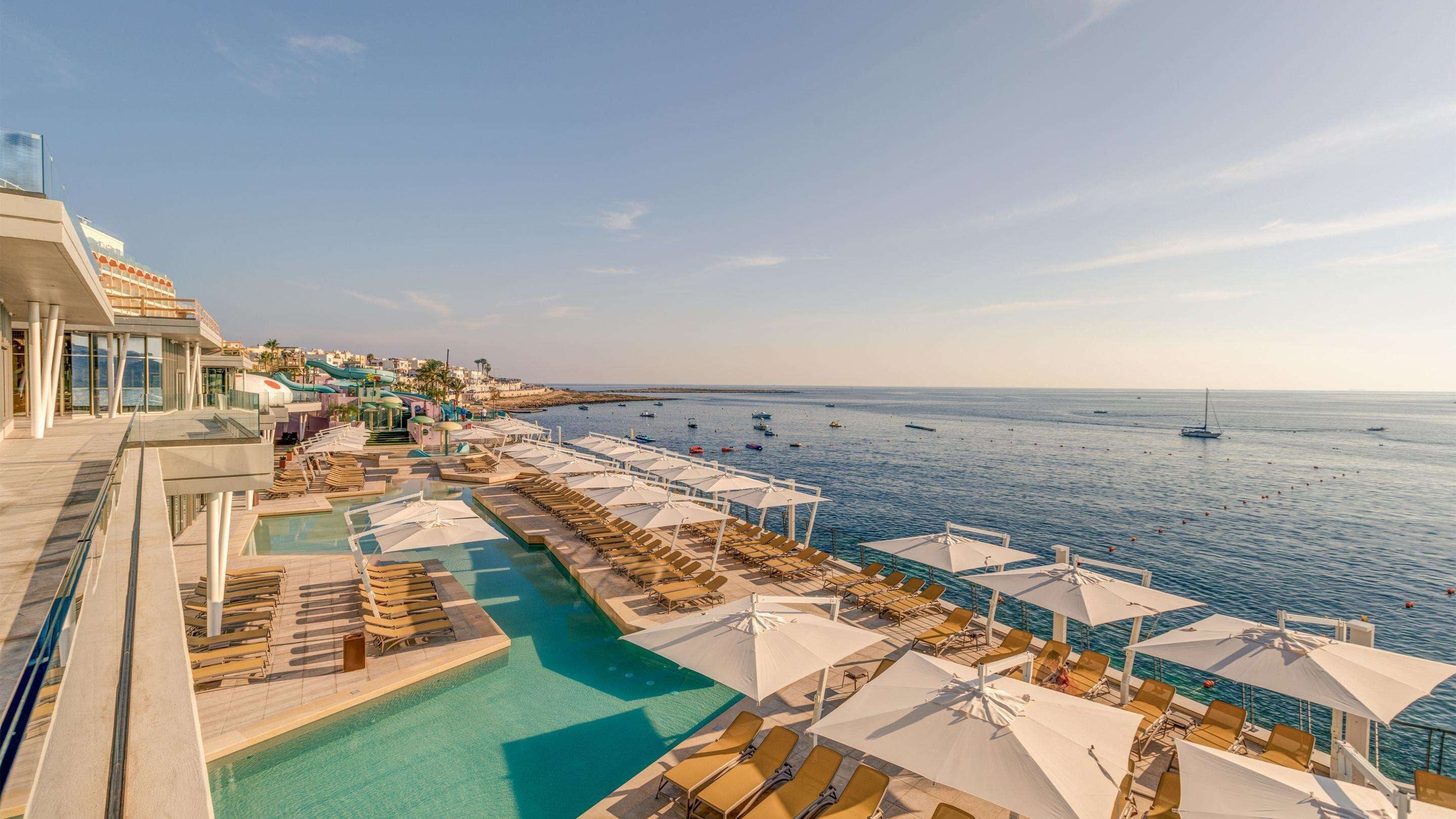 A resort with a pool area, sun loungers, and a view of the sea.