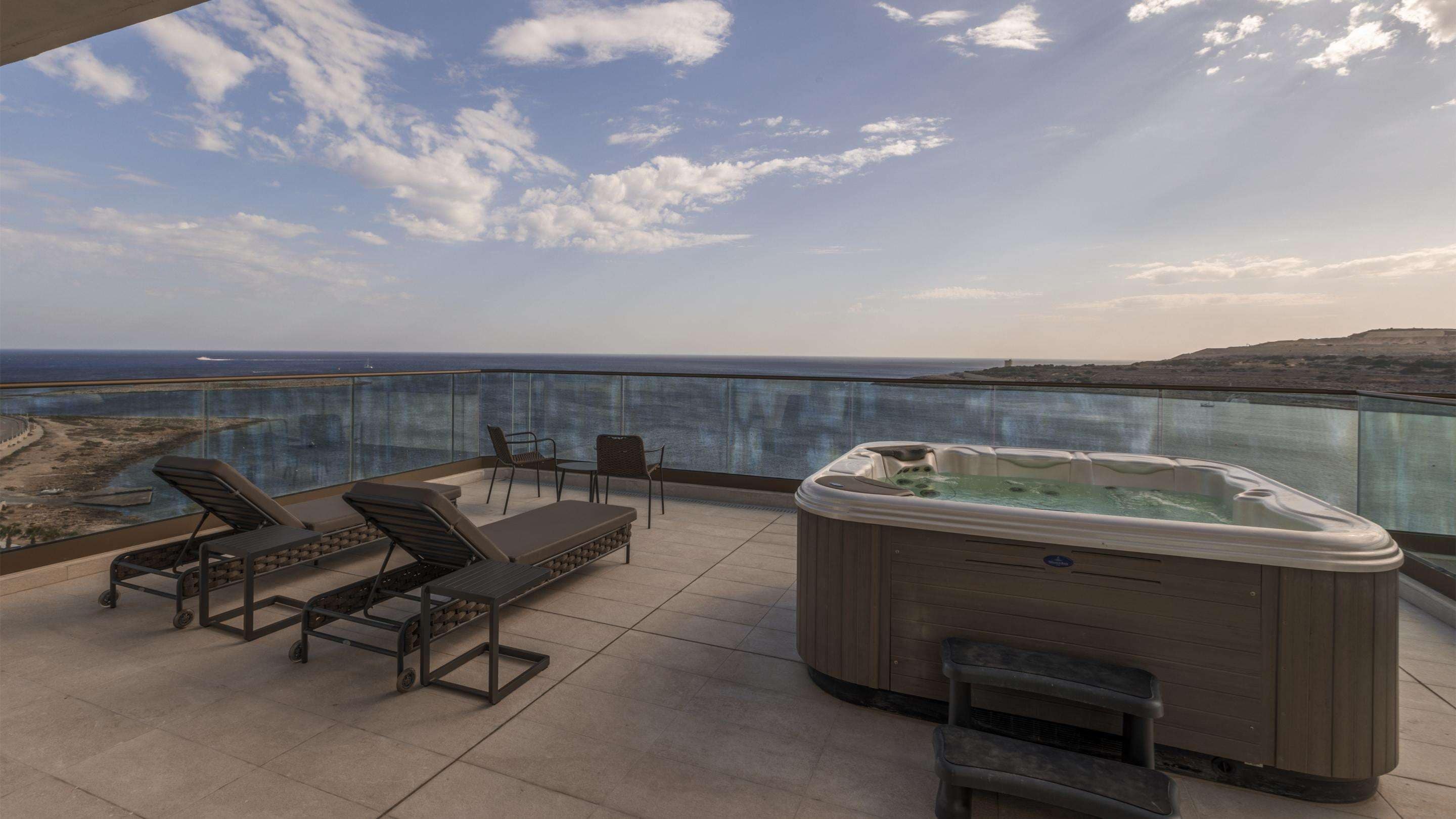A balcony with a hot tub, lounge chairs, and a view of the ocean.