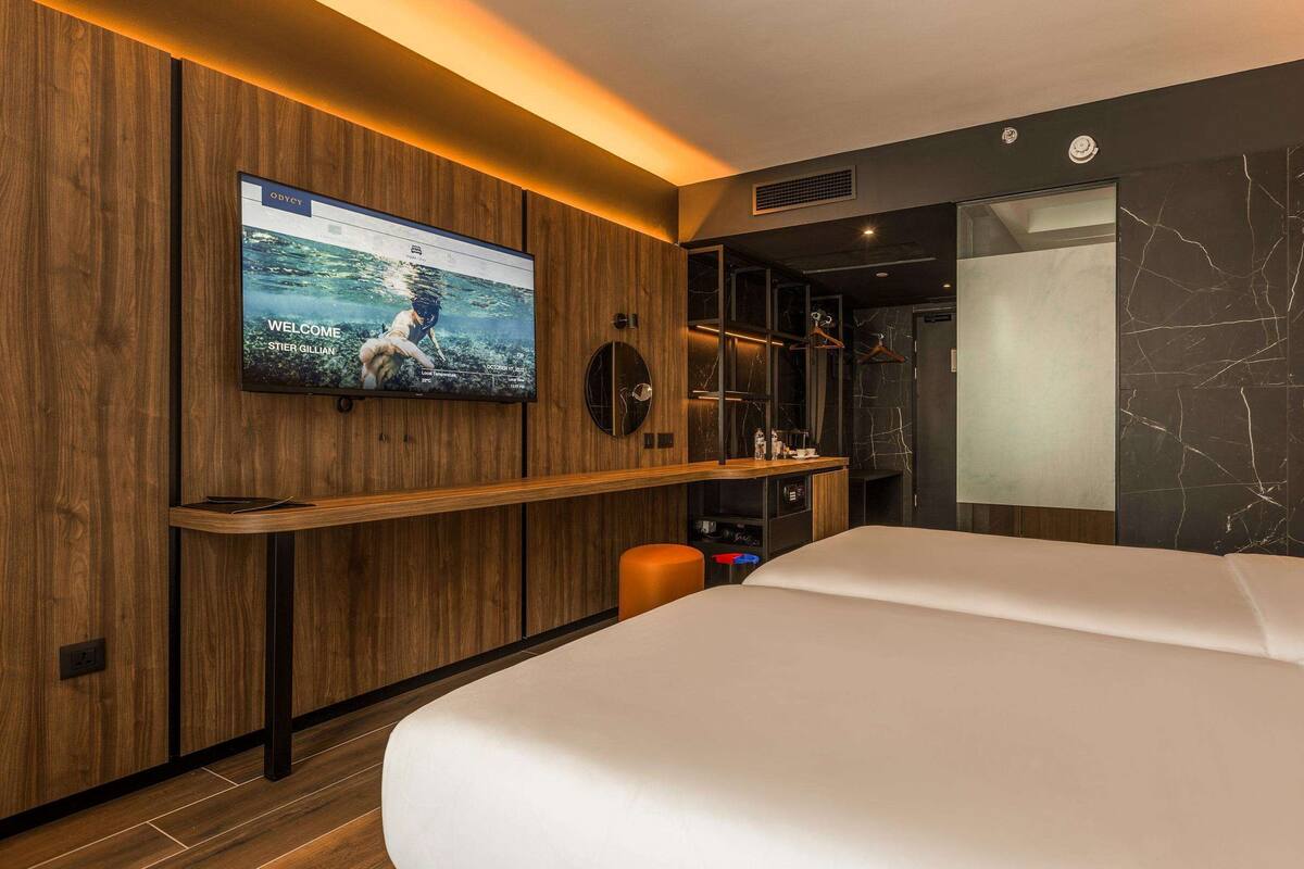 A modern hotel room with a large bed, a TV mounted on the wall, a wooden desk, and a marble wall.