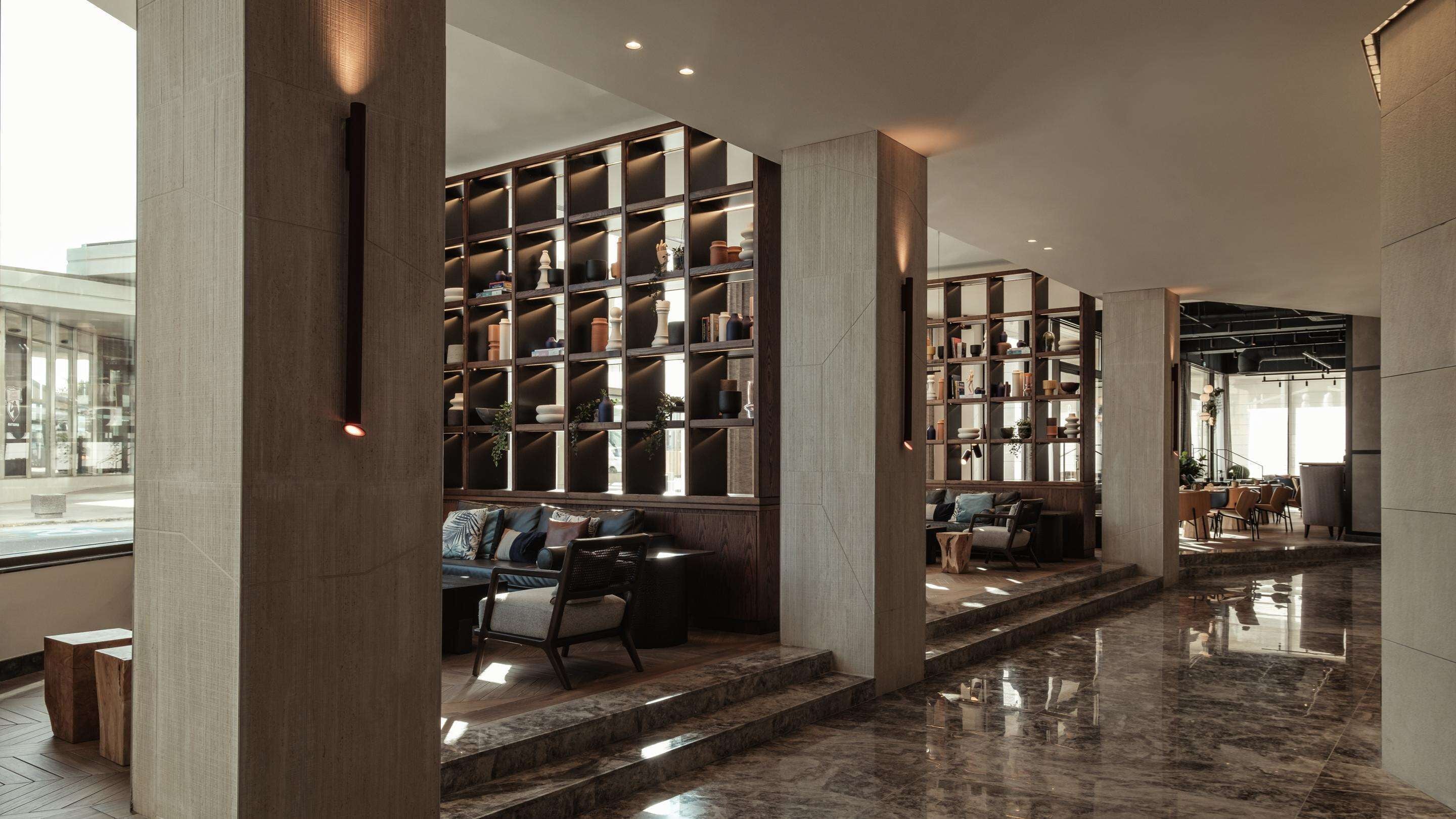 A modern interior with a central seating area, a large bookshelf, and a polished marble floor.
