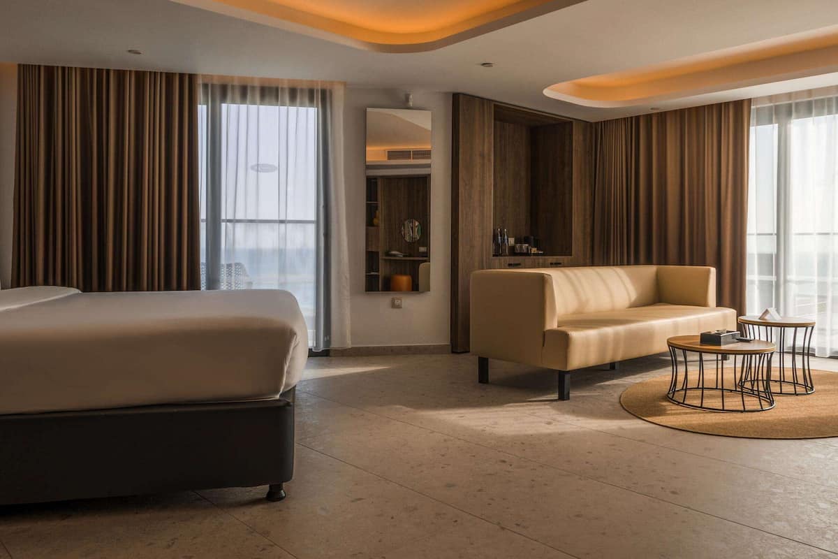 A modern hotel room with a large bed, a sofa, a small table, and a mirror.