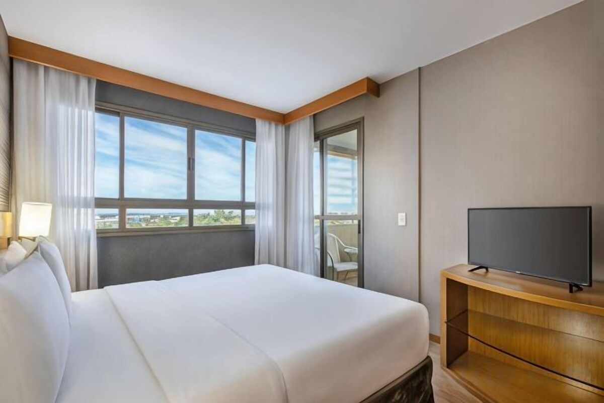Une chambre d’hôtel avec un lit, un téléviseur posé sur un meuble en bois et une fenêtre avec des rideaux.