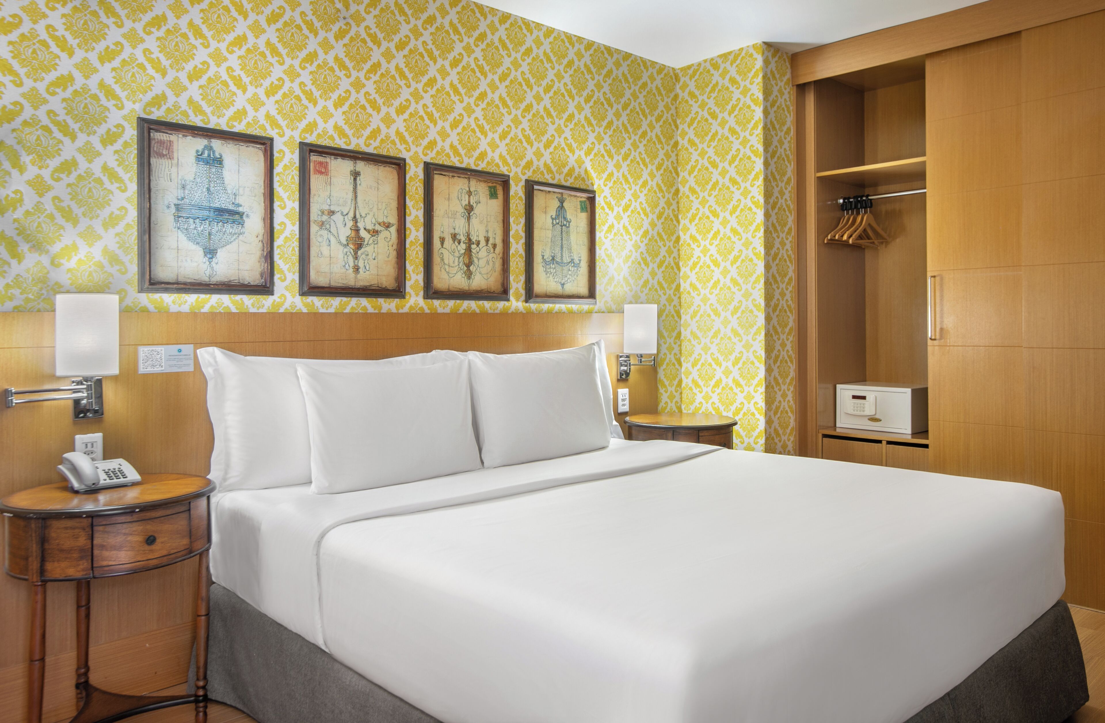 A hotel room with a large bed, bedside tables, a wardrobe, and wall-mounted artwork.
