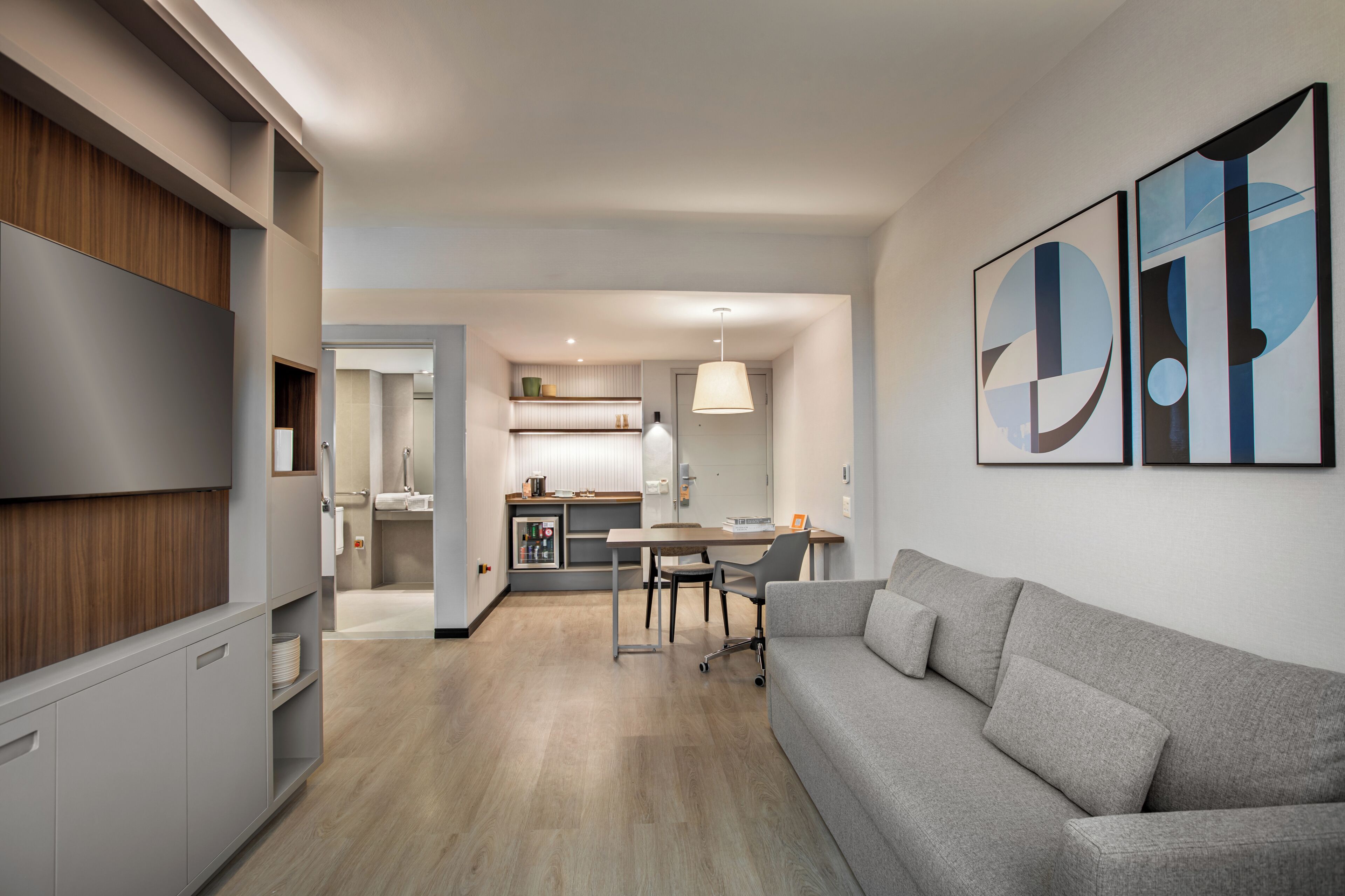 A modern living room with a grey sofa, a dining table, and a kitchen area in the background.