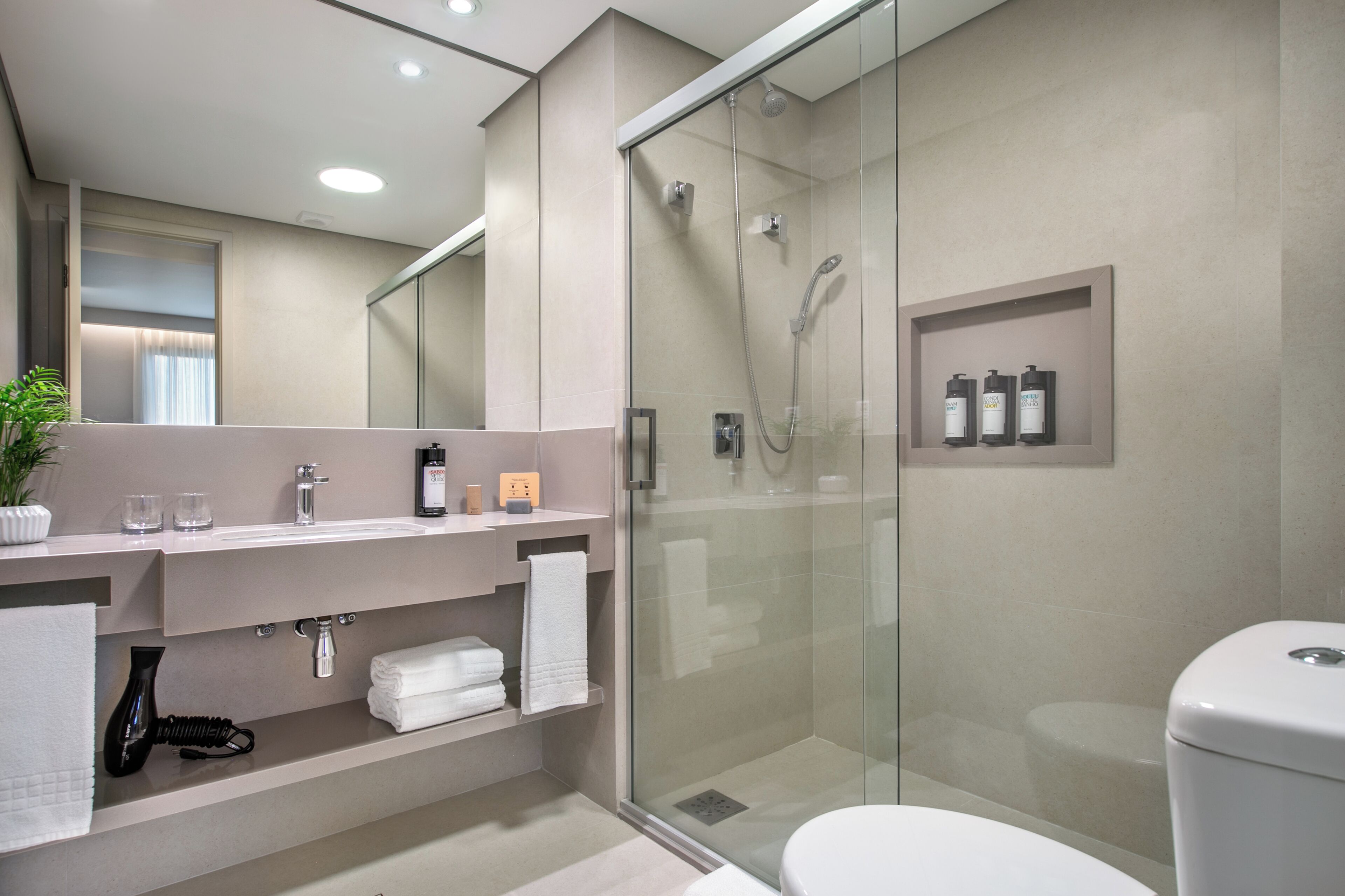 A modern bathroom with a glass-enclosed shower, a white toilet, and a vanity with a mirror and towel rack.