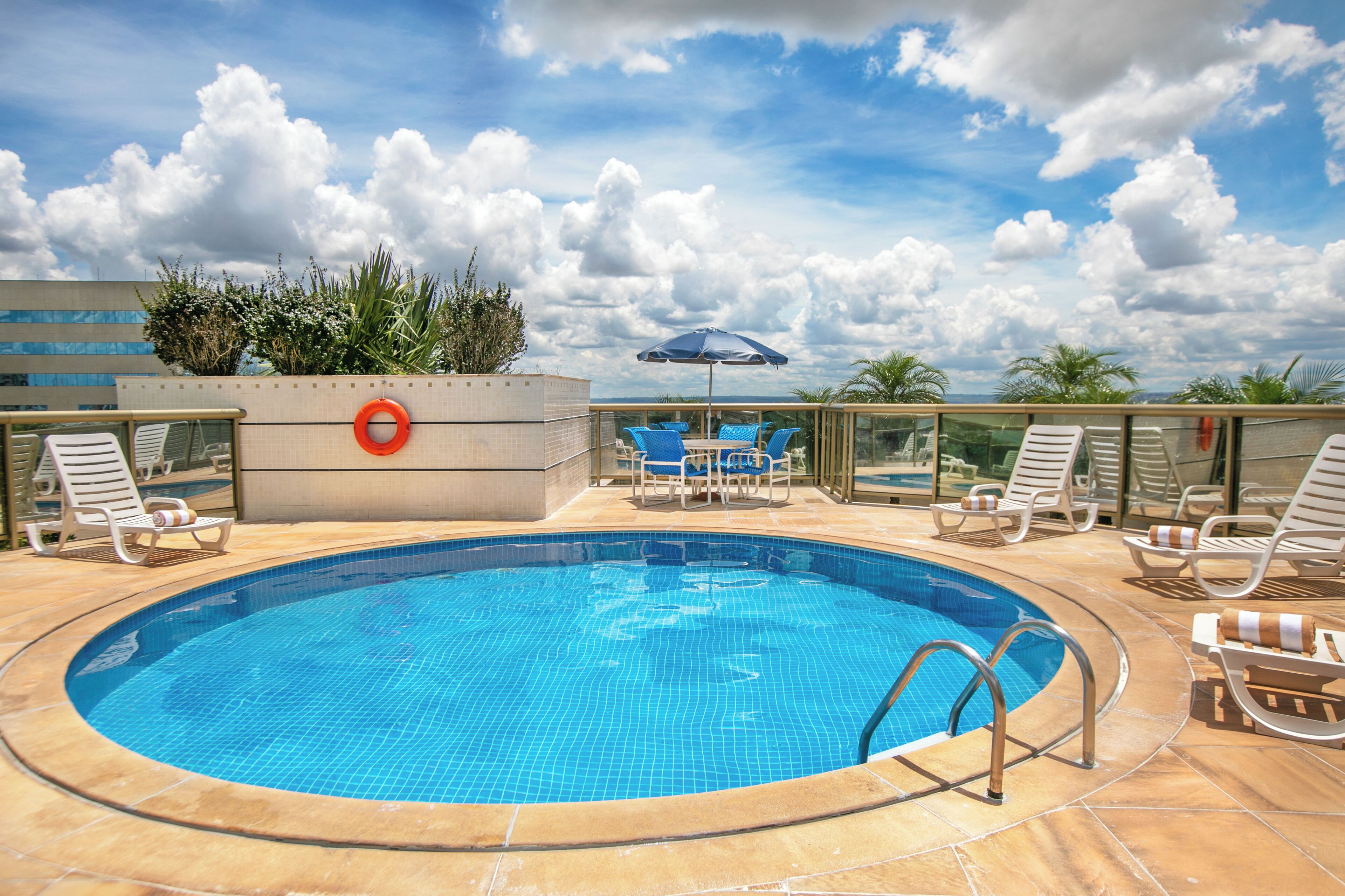 A rooftop swimming pool with lounge chairs and a blue umbrella.