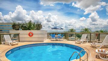 A rooftop swimming pool with lounge chairs and a blue umbrella.