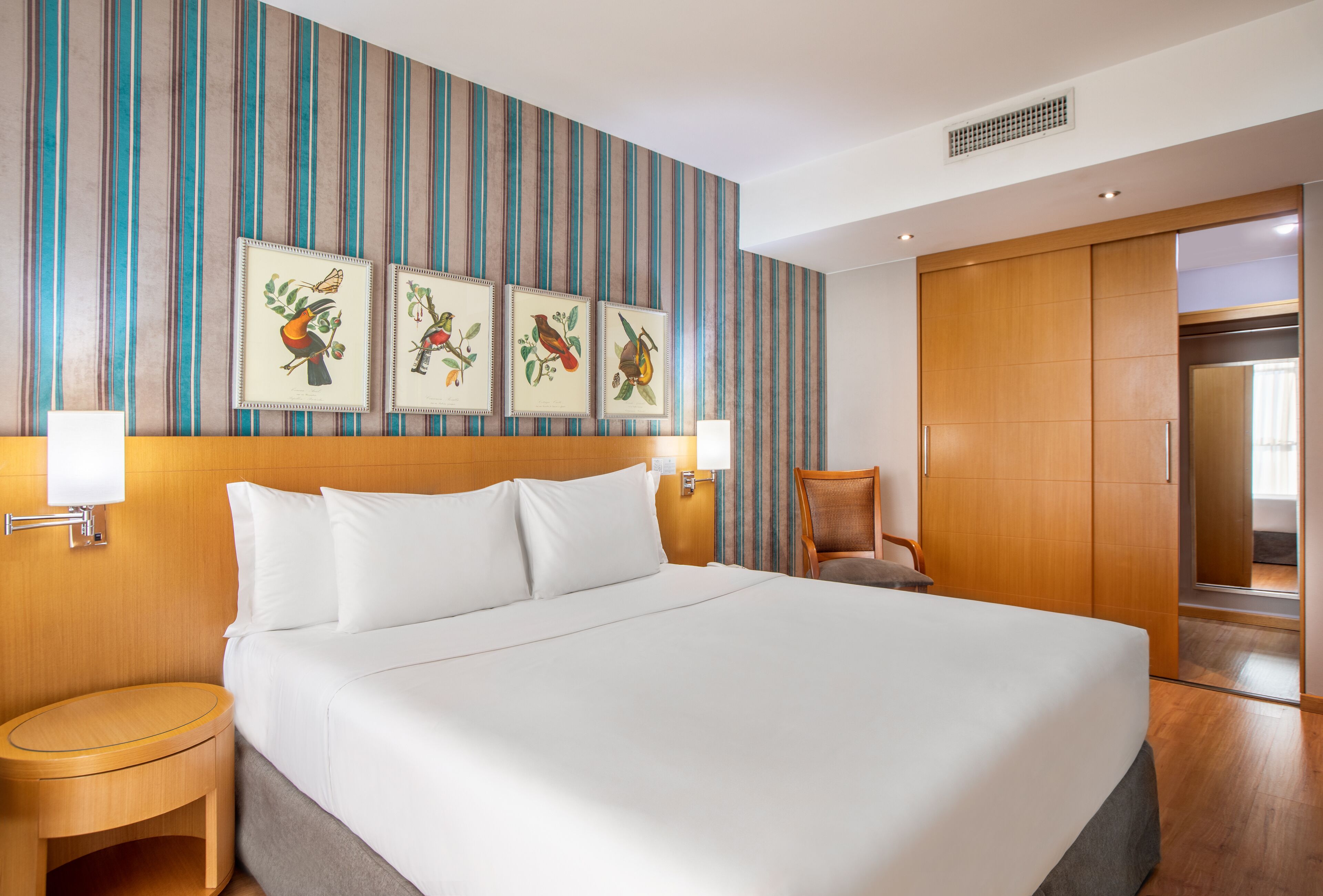 Ein Hotelzimmer mit einem großen Bett, einem Nachttisch aus Holz, einem Sessel und einem Kleiderschrank.