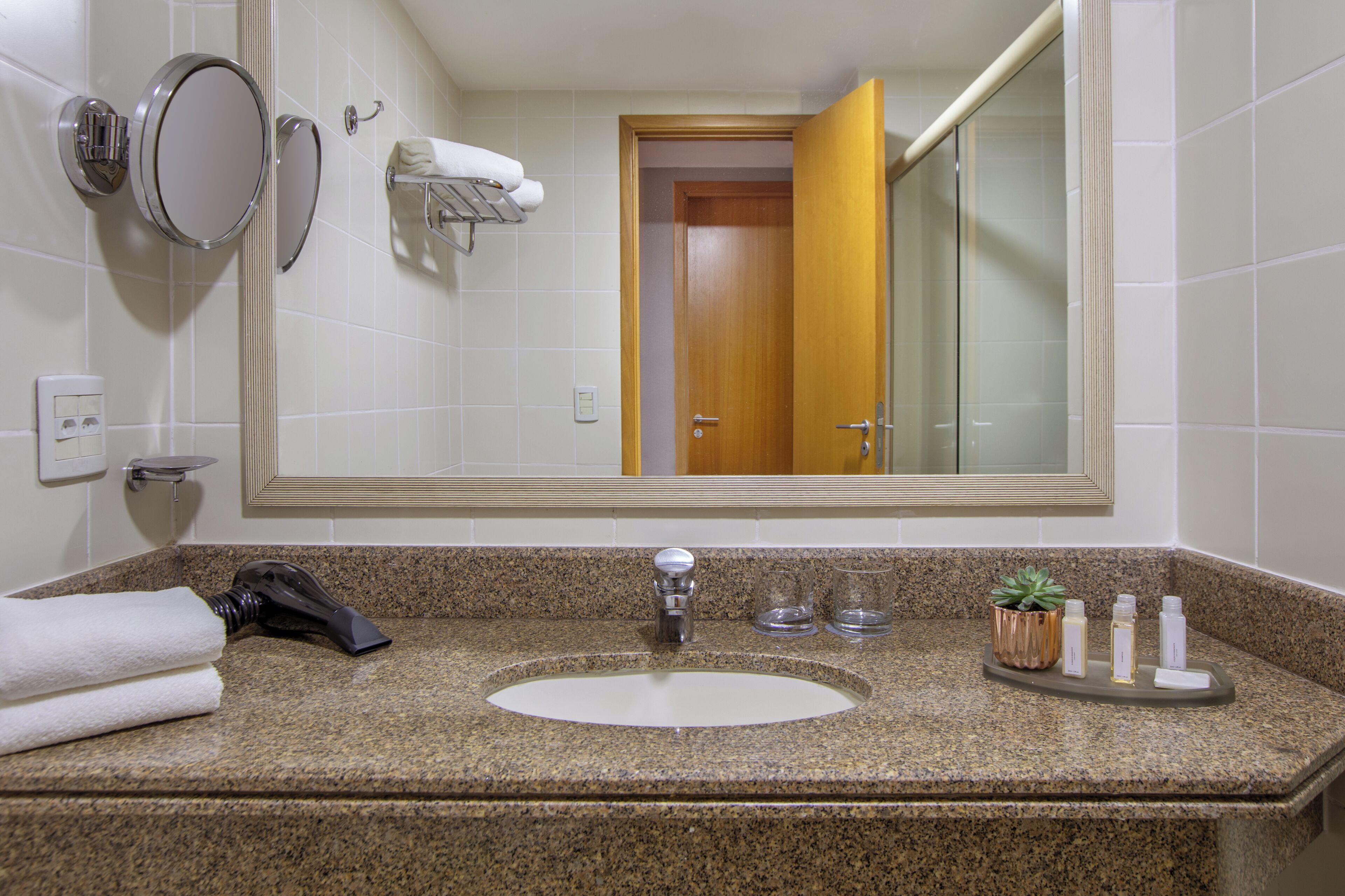 Une salle de bain dotée d’un comptoir en granit, d’un lavabo, d’un miroir, d’un porte-serviettes et d’une porte donnant sur une autre pièce.