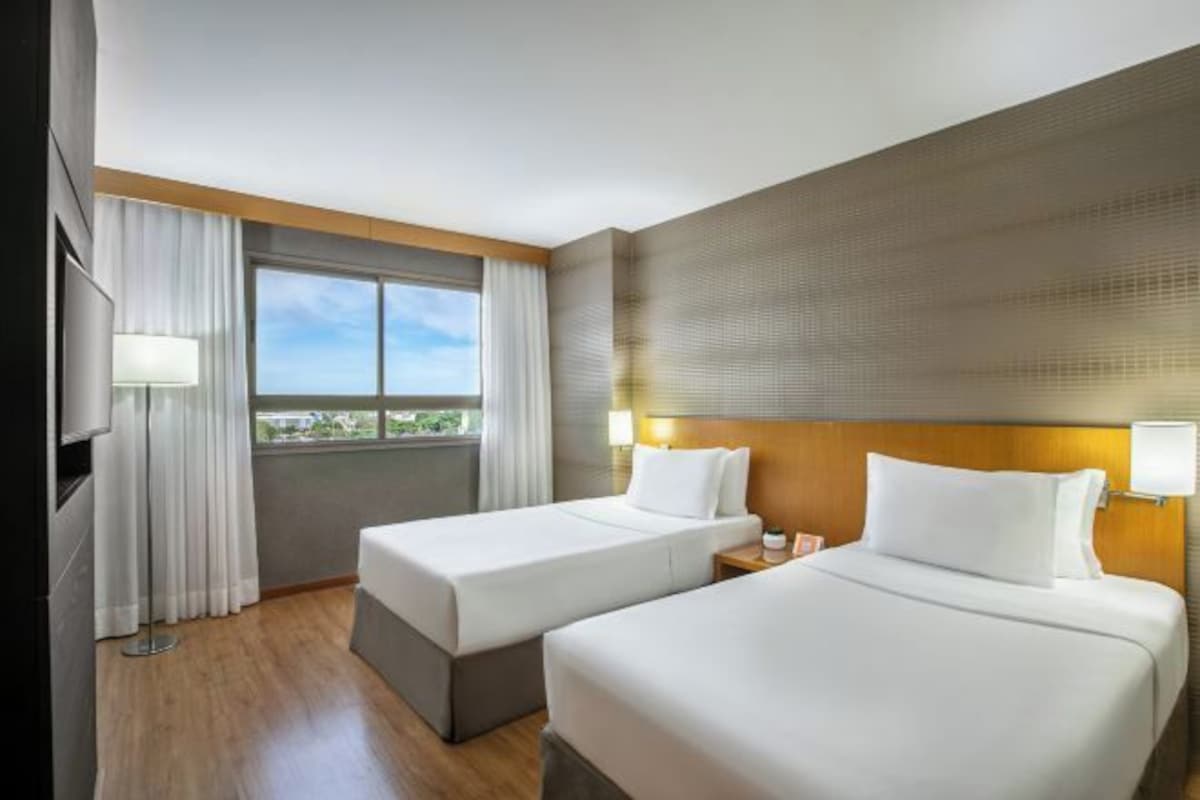 Une chambre d’hôtel avec deux lits, une télévision, une fenêtre avec des rideaux et une vue sur l’extérieur.