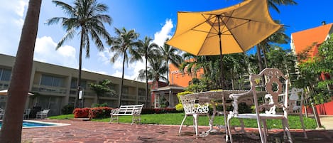 Un patio con piscina, mobiliario exterior, palmeras y un edificio con un cartel que dice "POSADA DEL".