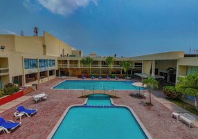 Zona de piscina de hotel con varias piscinas, sillas de descanso y un área de estar cubierta.