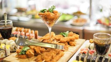 A buffet with various food items including sushi, skewered meat, and a martini glass with a drink.