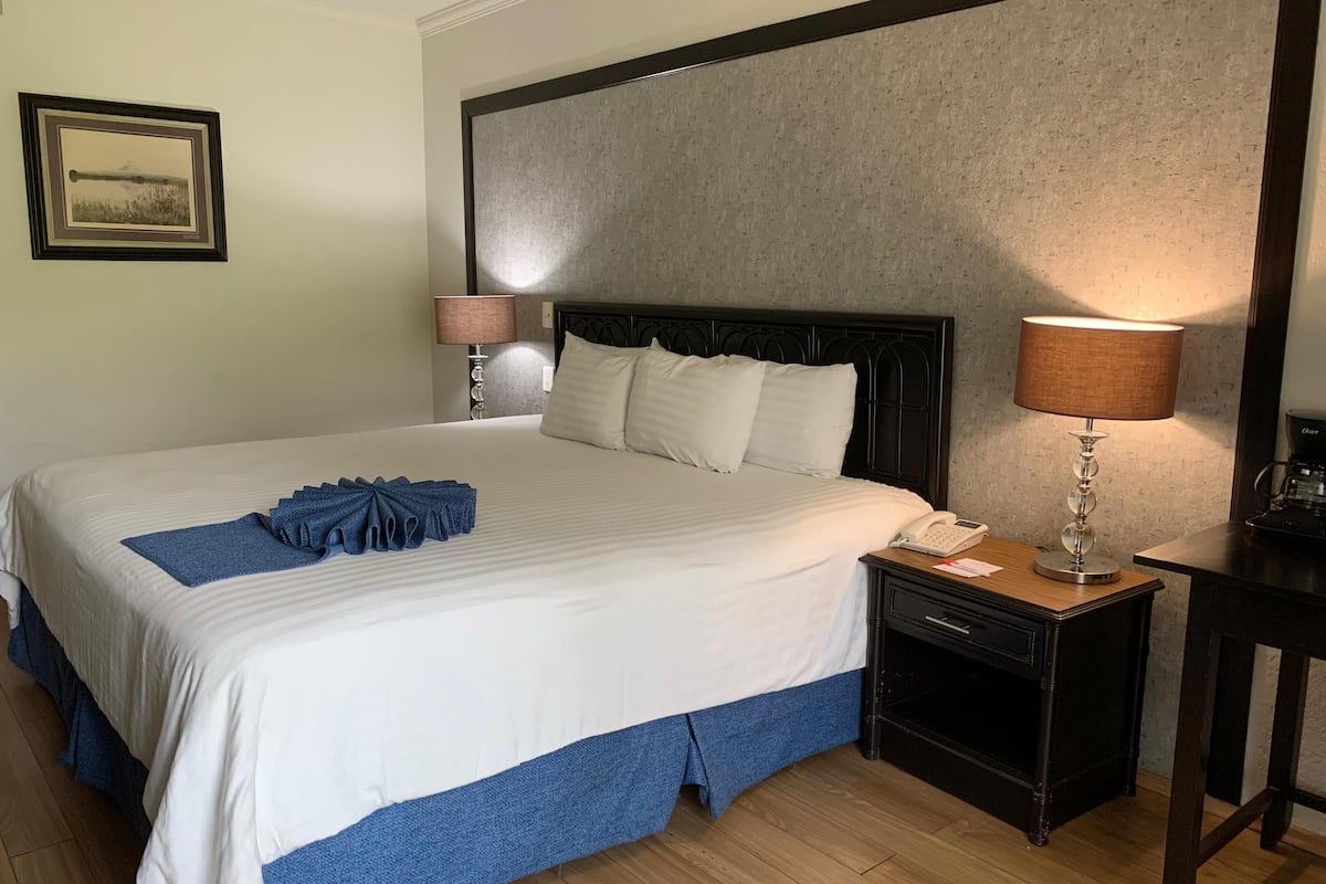 Una cama bien hecha con falda azul, una lámpara de noche y un teléfono en la mesita.